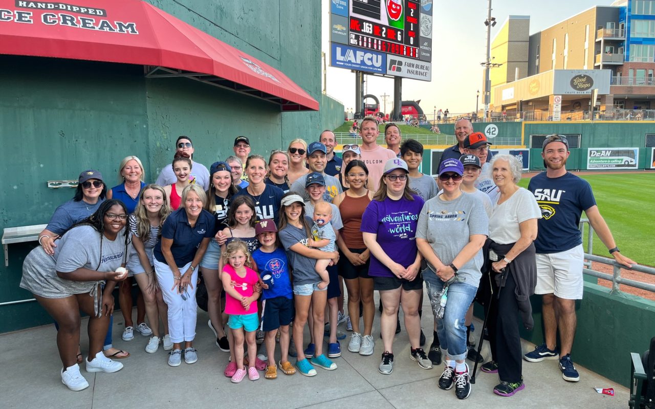 Group of alumni at a Lugnuts baseball game posing by the field.