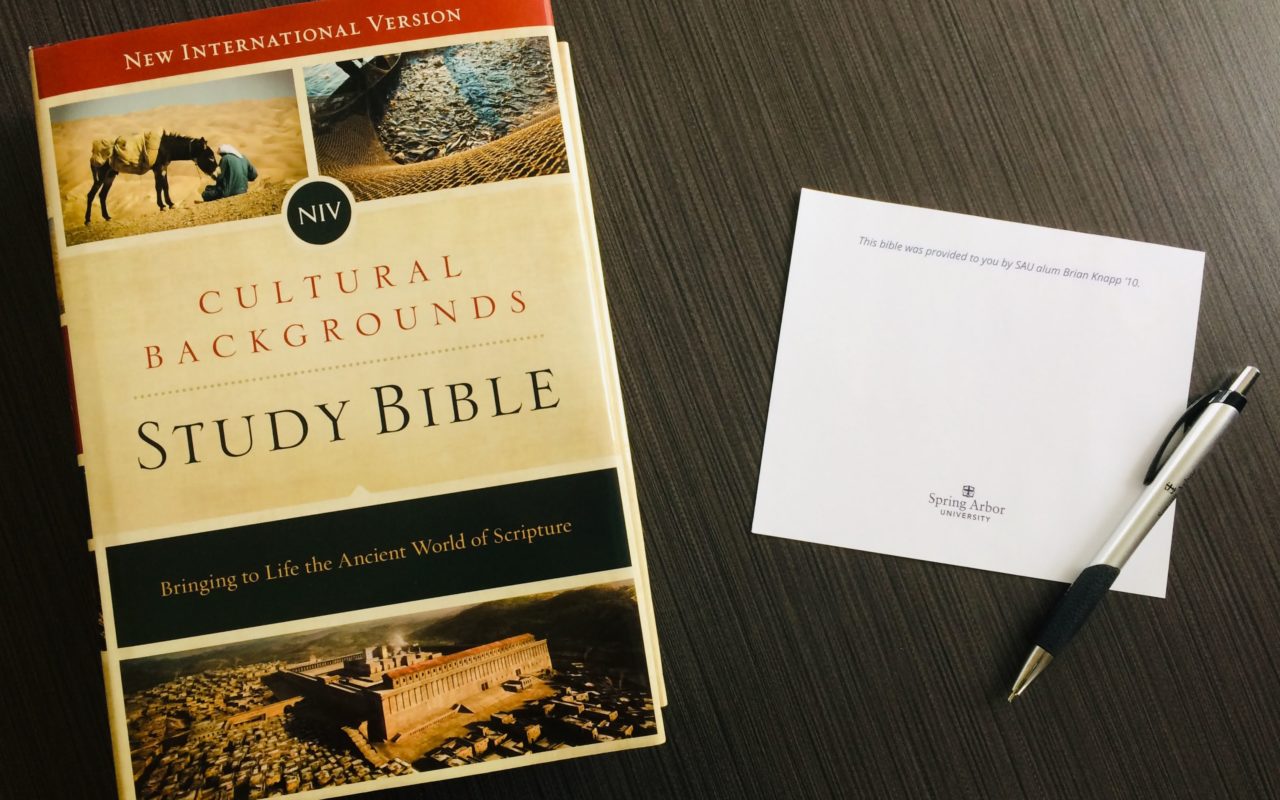 A study Bible and notecard on a table with a pen.