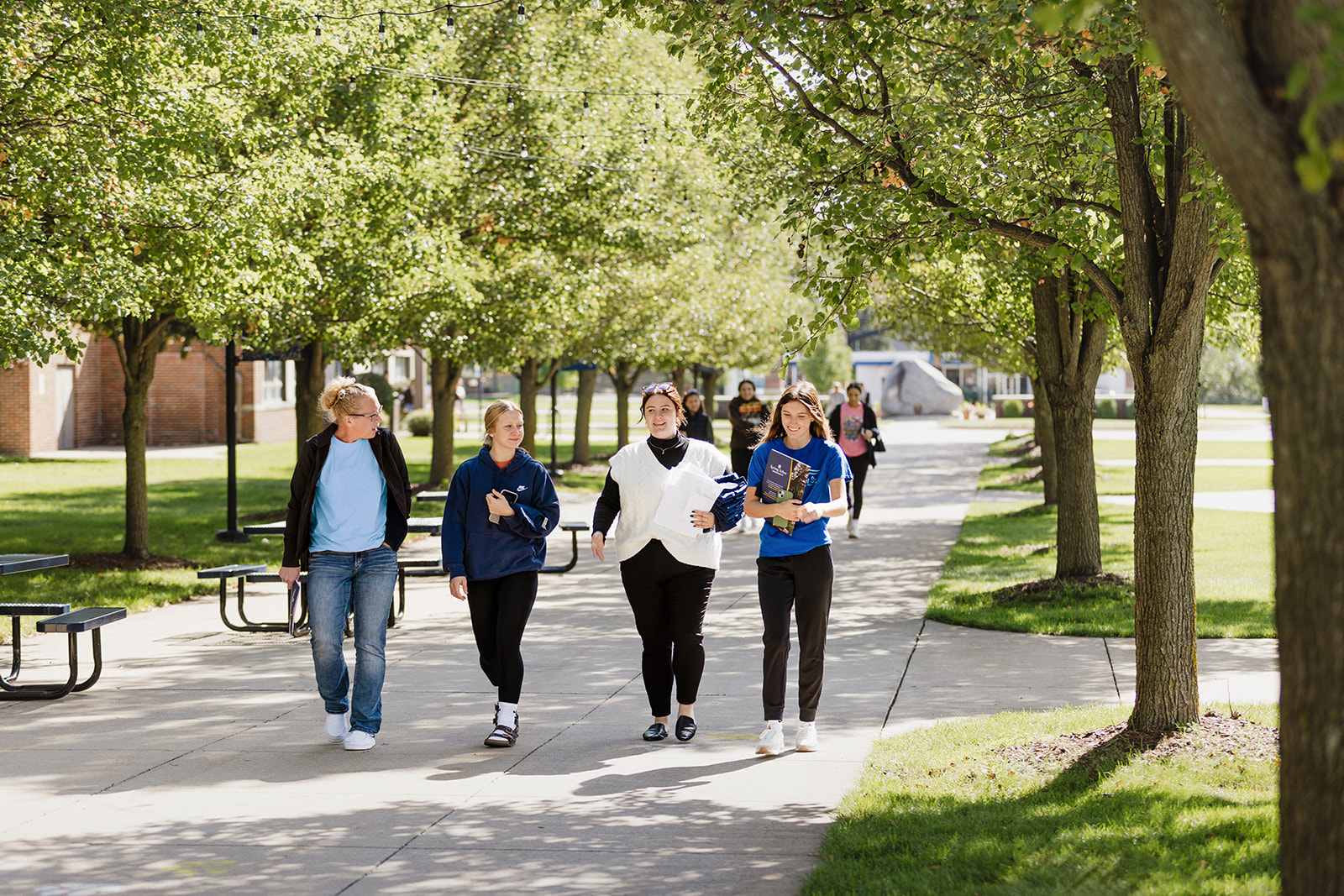 A group of students on a tour of campus. Walking on the sidewalk talking and laughing with blossoms on the trees on a bright, Spring day.