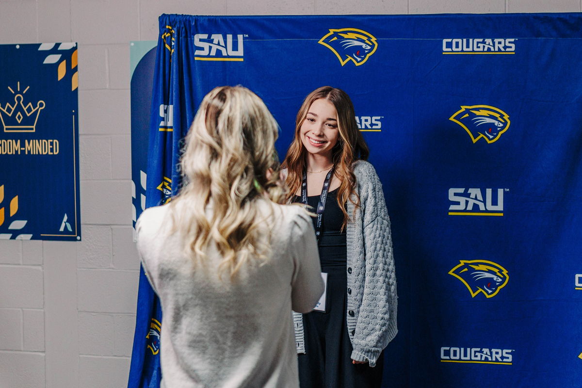 Prospective student smiling for picture in front of SAU banner.
